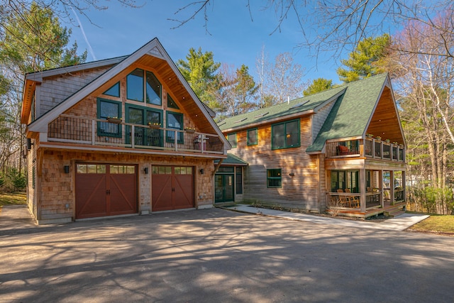rustic home featuring driveway, a balcony, a shingled roof, and a garage