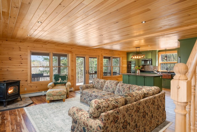 living area with baseboard heating, a wood stove, a wealth of natural light, and wood ceiling
