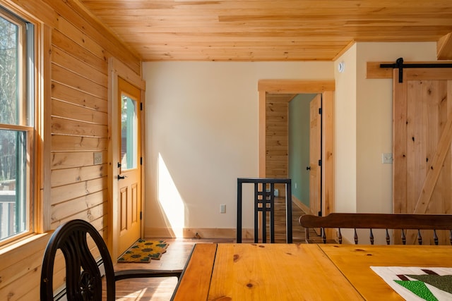 dining space with wooden ceiling, wood walls, a barn door, and a healthy amount of sunlight