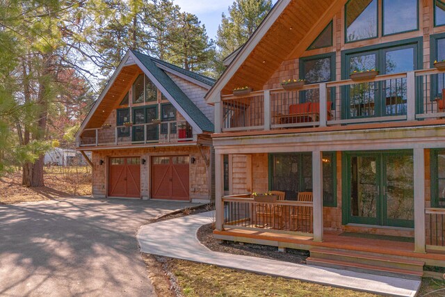 rear view of house featuring french doors, aphalt driveway, a balcony, and an attached garage