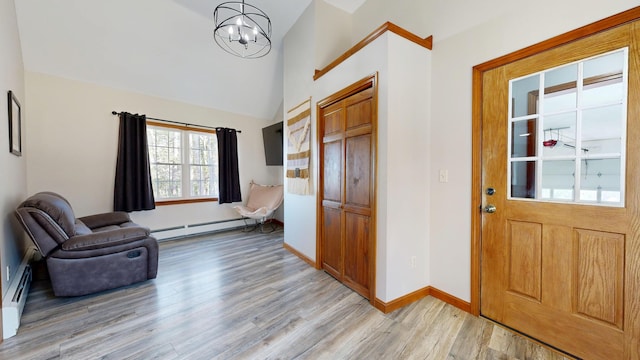 foyer entrance with an inviting chandelier, baseboard heating, light wood finished floors, high vaulted ceiling, and baseboards