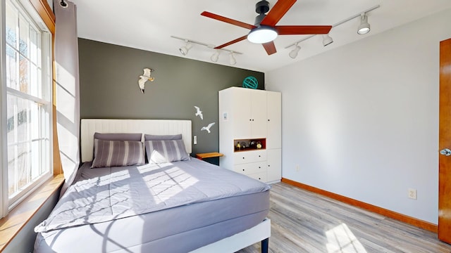 bedroom featuring track lighting, baseboards, light wood-type flooring, and ceiling fan