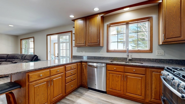 kitchen featuring brown cabinetry, a sink, dark stone countertops, a peninsula, and stainless steel appliances