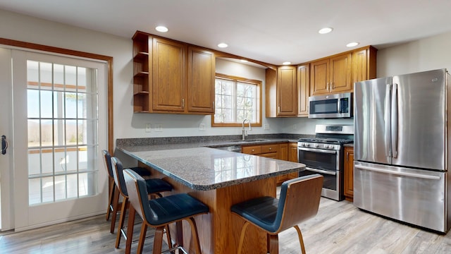 kitchen featuring brown cabinets, open shelves, appliances with stainless steel finishes, a sink, and a kitchen bar