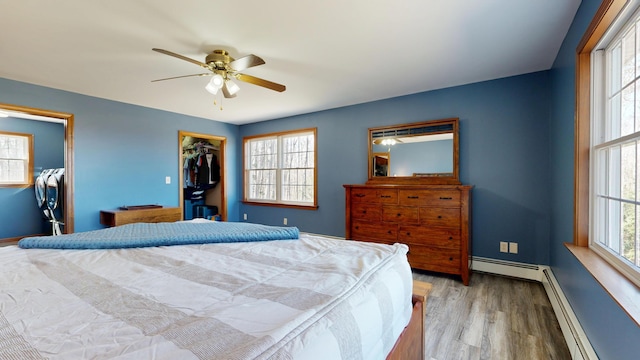 bedroom featuring baseboards, a walk in closet, wood finished floors, and a baseboard radiator