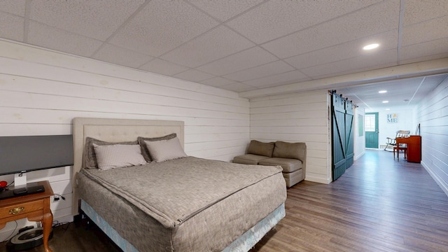 bedroom featuring wood finished floors, wooden walls, recessed lighting, a barn door, and a paneled ceiling