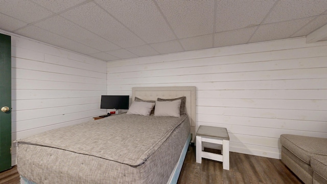 bedroom featuring wood walls, dark wood-style flooring, and a paneled ceiling