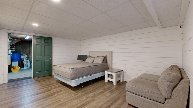 bedroom with a paneled ceiling, wood walls, and wood finished floors