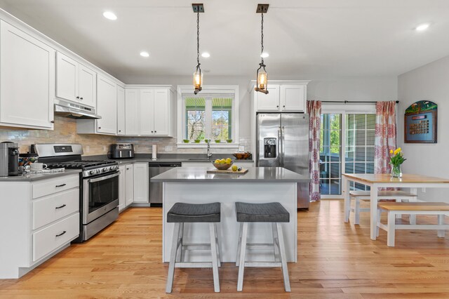 kitchen with backsplash, white cabinets, under cabinet range hood, a breakfast bar, and stainless steel appliances