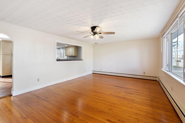 empty room featuring a baseboard radiator, arched walkways, ceiling fan, and light wood finished floors