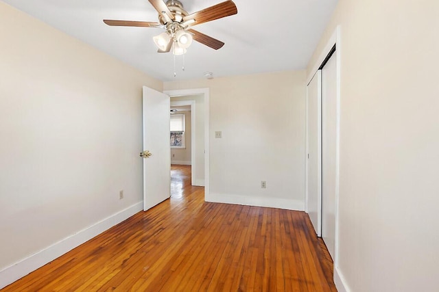 unfurnished bedroom with baseboards, a ceiling fan, hardwood / wood-style floors, and a closet