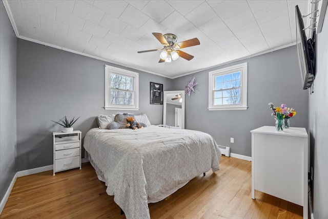 bedroom with wood finished floors, ornamental molding, and multiple windows