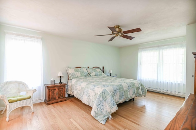 bedroom featuring ceiling fan, multiple windows, a baseboard radiator, and light wood-style floors