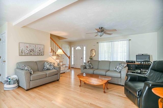 living area with baseboard heating, light wood finished floors, a ceiling fan, and stairs