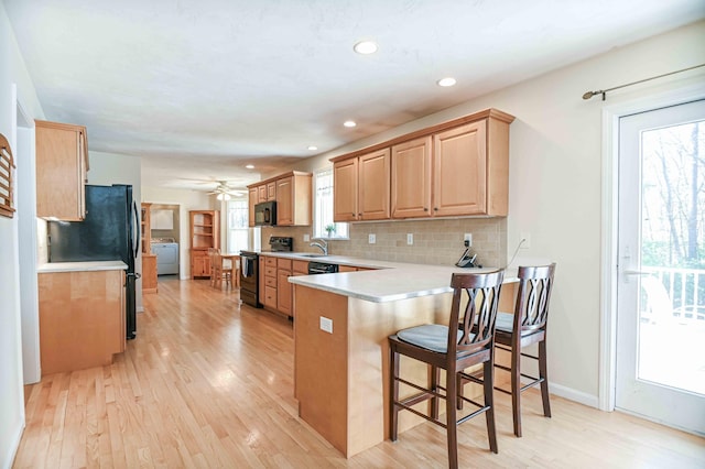 kitchen featuring a peninsula, light brown cabinetry, light wood-style floors, light countertops, and black appliances