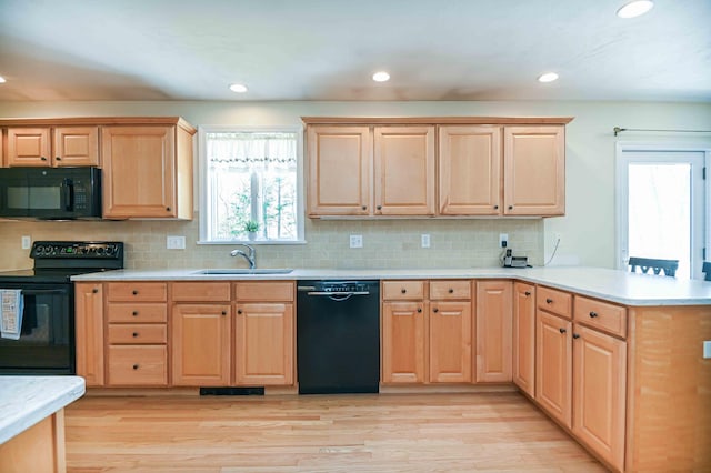 kitchen with a sink, light countertops, black appliances, a peninsula, and light brown cabinets