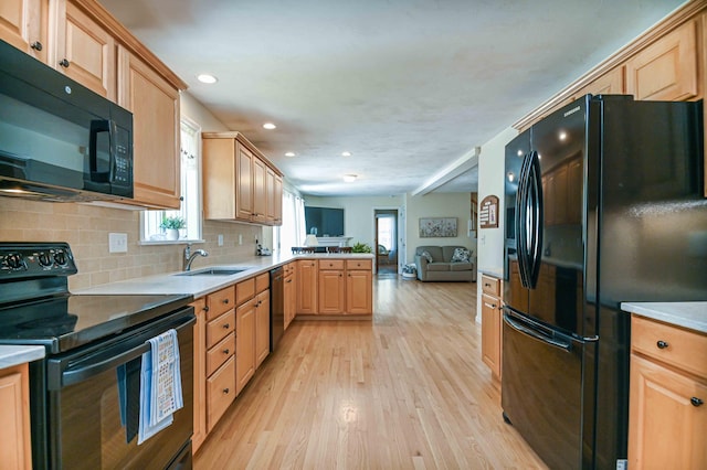 kitchen with light brown cabinetry, a sink, black appliances, open floor plan, and light wood-style flooring