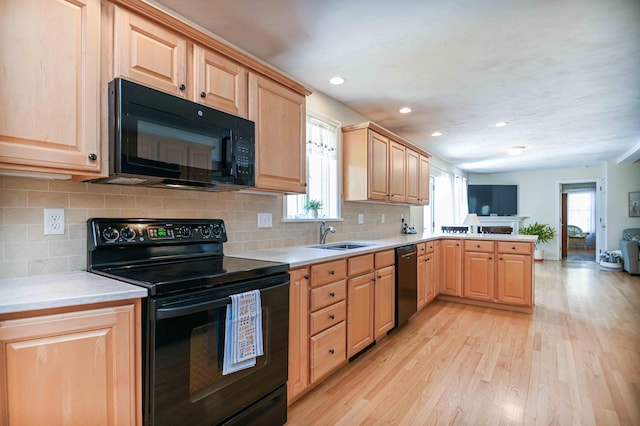 kitchen featuring a sink, light wood-style floors, light brown cabinets, a peninsula, and black appliances