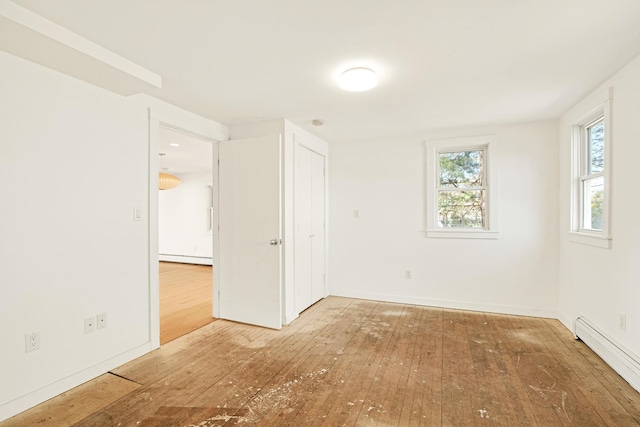empty room with wood-type flooring, a baseboard radiator, and baseboards