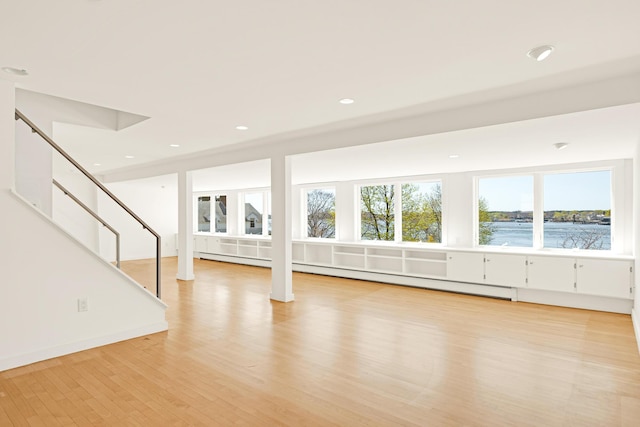 unfurnished living room with light wood-style floors, recessed lighting, a baseboard heating unit, and stairs