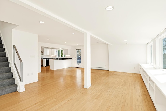 unfurnished living room with recessed lighting, a baseboard heating unit, stairway, and light wood-type flooring