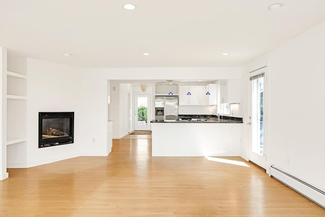 kitchen featuring dark countertops, baseboard heating, light wood-type flooring, stainless steel fridge with ice dispenser, and a peninsula