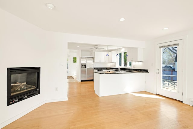 kitchen with light wood-style floors, dark countertops, a peninsula, stainless steel fridge, and white cabinetry