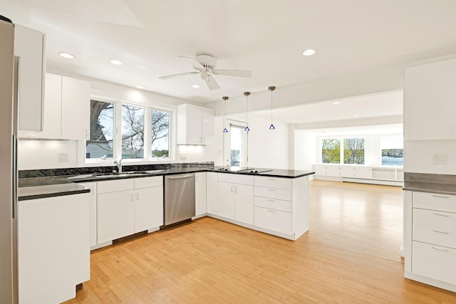 kitchen featuring dark countertops, stainless steel dishwasher, a sink, white cabinets, and a peninsula