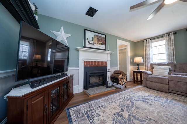219 Middle Rd, Skowhegan, ME 04976 - living room with wood finished floors, a brick fireplace, ceiling fan, a wainscoted wall, and a baseboard radiator