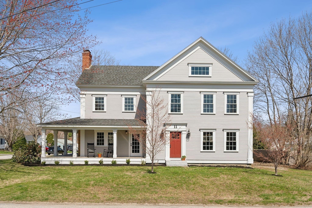 view of front facade with a front lawn, a chimney, covered porch, and roof with shingles