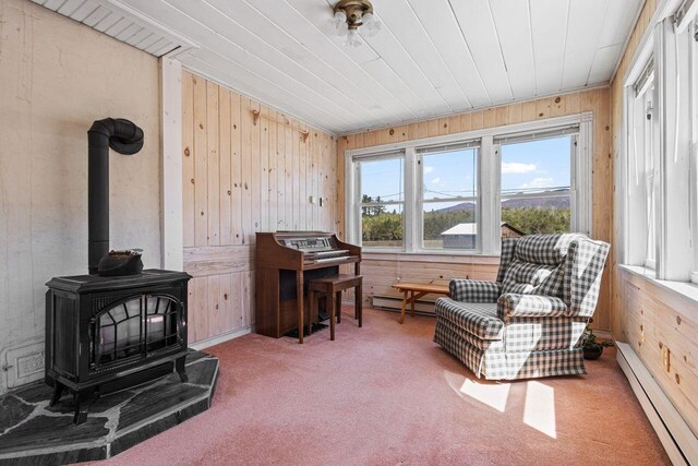 living area with a baseboard heating unit, carpet flooring, a wood stove, and wooden walls