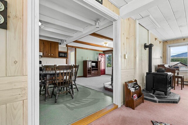 carpeted dining room featuring wooden walls, a wood stove, and vaulted ceiling with beams
