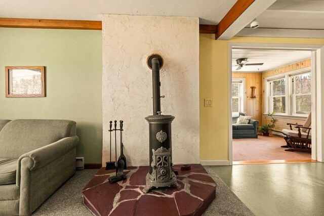 living room with a wood stove, a ceiling fan, beamed ceiling, baseboards, and baseboard heating