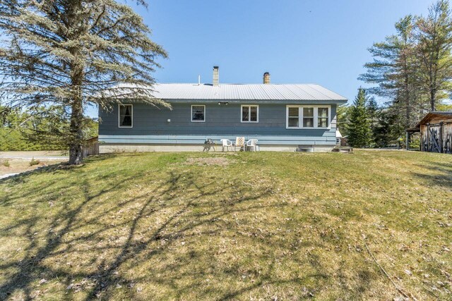 back of house featuring a chimney, a yard, and metal roof