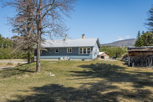 back of house with a chimney, a mountain view, metal roof, and a lawn
