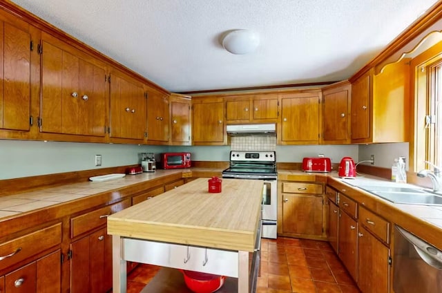kitchen featuring a textured ceiling, under cabinet range hood, brown cabinets, and stainless steel appliances
