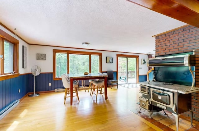 dining room featuring ornamental molding, wood finished floors, baseboard heating, a textured ceiling, and a wainscoted wall
