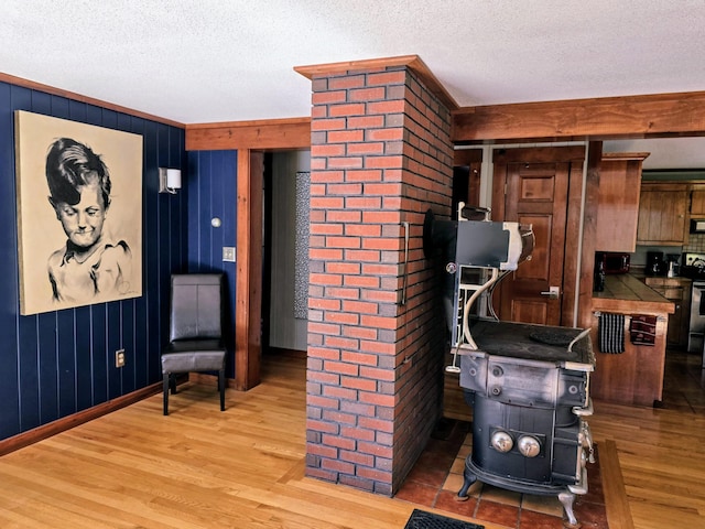 interior space with a textured ceiling, wood walls, wood finished floors, and a wood stove