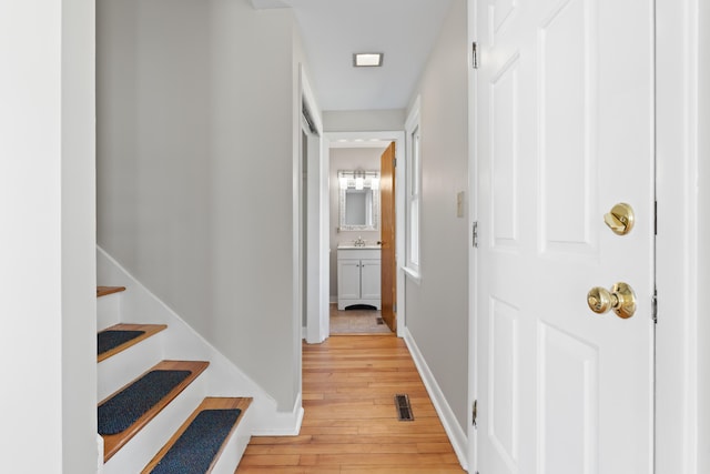 hallway with light wood-style floors, baseboards, a sink, and visible vents