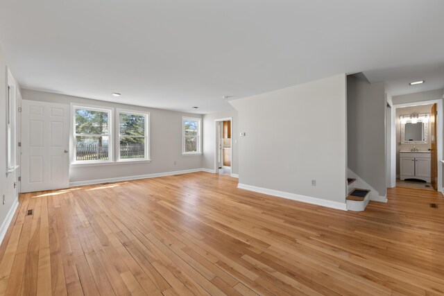 unfurnished living room with baseboards, light wood-style flooring, stairs, and visible vents