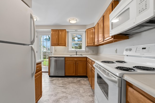 kitchen featuring white appliances, brown cabinetry, a sink, and light countertops