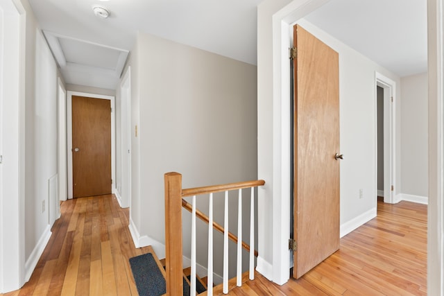 hallway with attic access, baseboards, an upstairs landing, and light wood finished floors