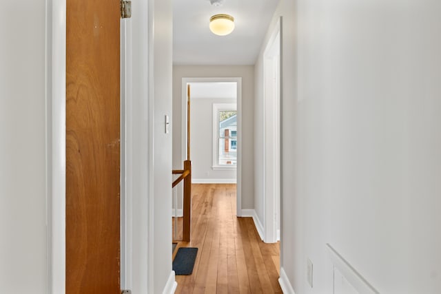 corridor with baseboards, an upstairs landing, and light wood-style floors