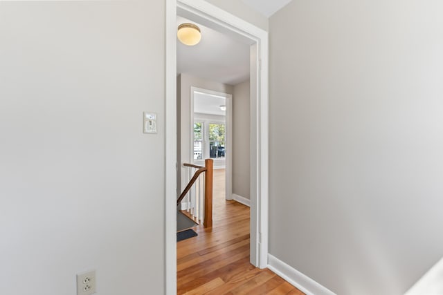 corridor featuring baseboards, light wood-type flooring, and an upstairs landing