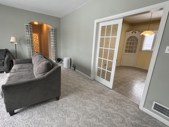 carpeted living room with arched walkways, baseboards, and visible vents