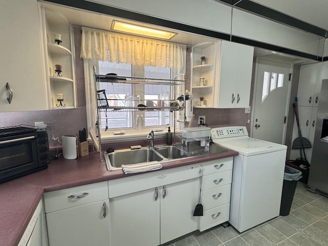 kitchen with white cabinets, a sink, dark countertops, open shelves, and washer / dryer