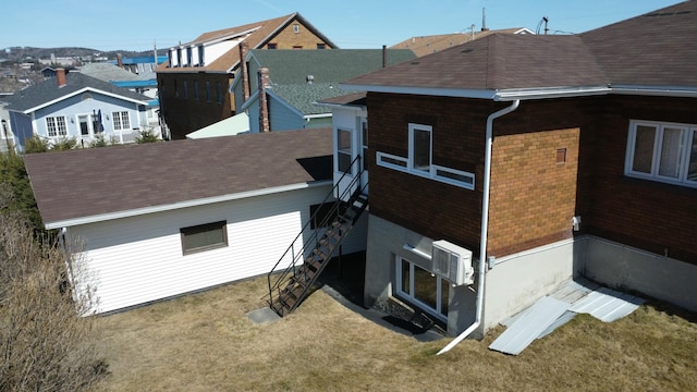 back of house with brick siding, a wall unit AC, and a shingled roof