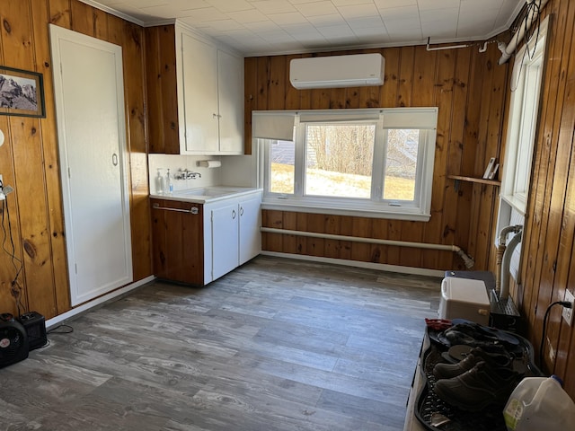 laundry room with wooden walls, wood finished floors, a wall unit AC, a sink, and cabinet space