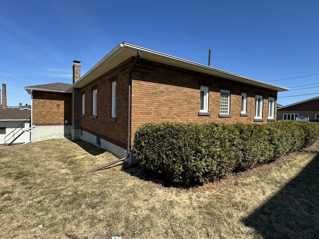 view of side of home featuring brick siding, a yard, and a chimney