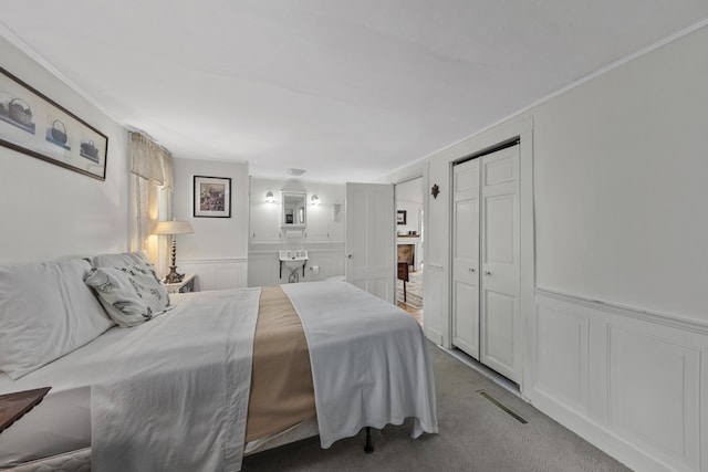 bedroom featuring a wainscoted wall, visible vents, carpet, a decorative wall, and connected bathroom